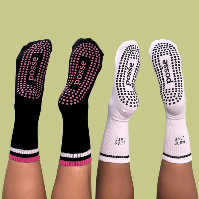 Flat lay of Posše grip socks in black and white with pink soles, showing motivational cuffs and dot grip soles
