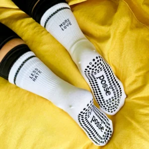 White grip socks with “More Love” and “Less Hate” cuffs, worn on yellow couch
