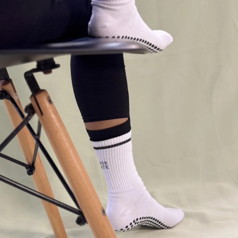 White Posše More Love grip socks with black silicone grip, worn on chair with legs crossed
