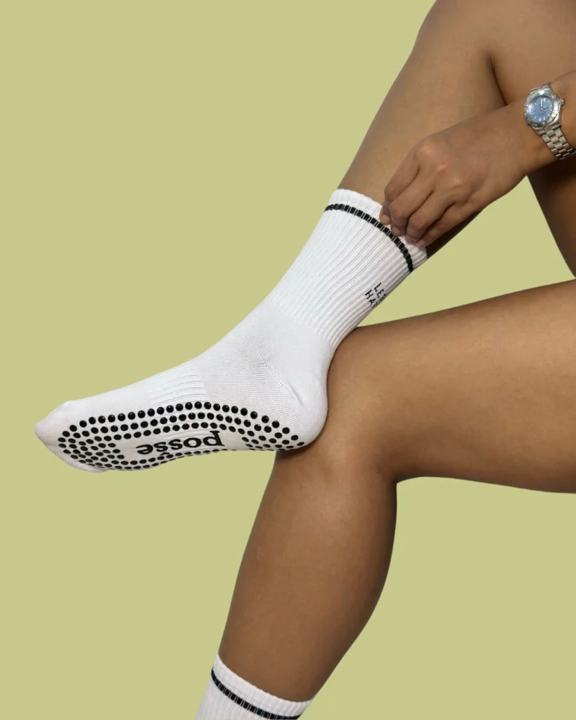 Posše white More Love grip socks with black soles, worn mid-leg lift over green background