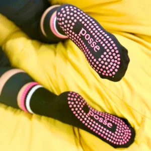 Black Posše grip socks with pink dots, soles facing up on yellow couch