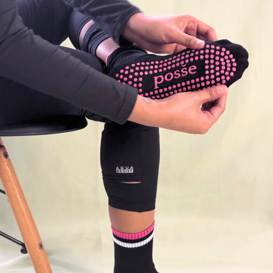osše No Chill black grip socks with pink soles, shown being stretched and held by a seated woman in leggings