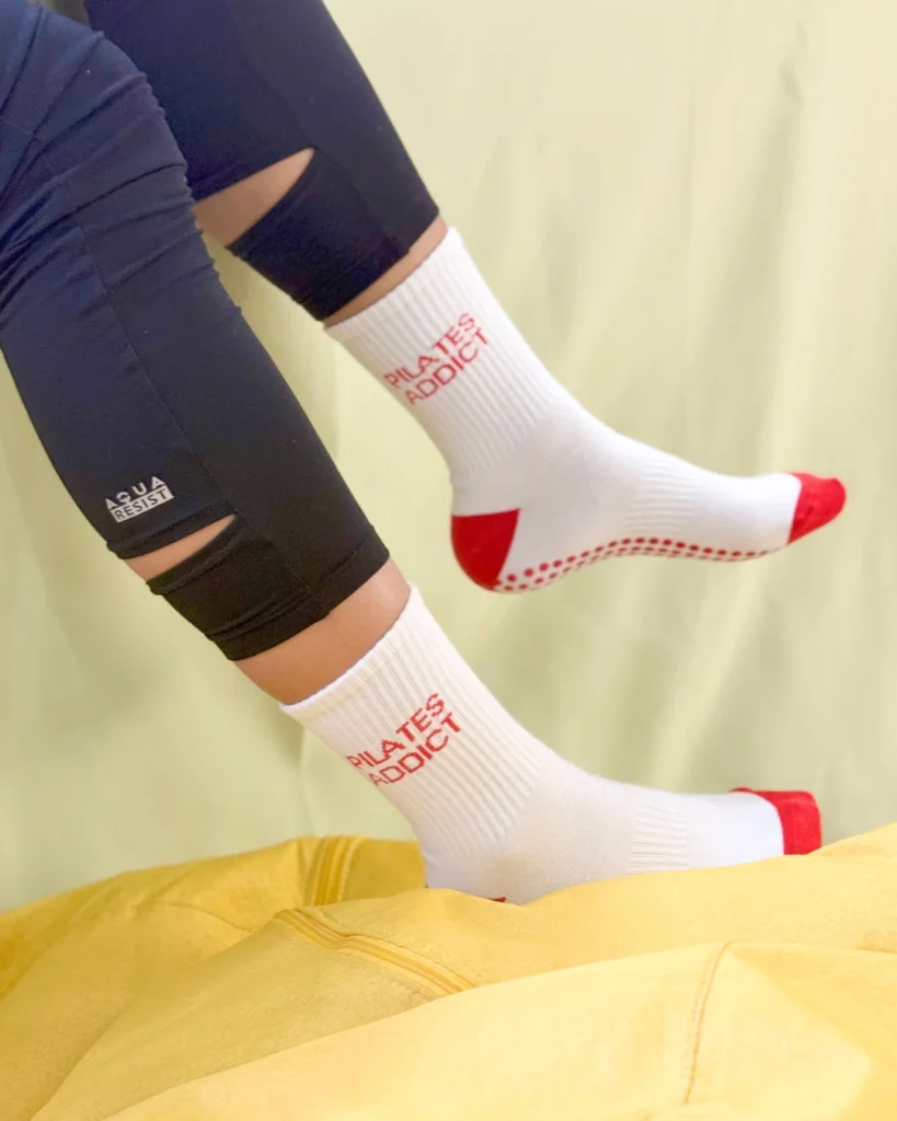 Posše Pilates Addict grip socks in white and red, worn mid-air over yellow cushion